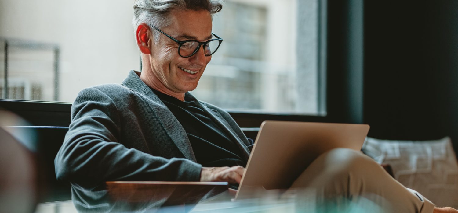 The picture shows a young man sitting behind his laptop and working.